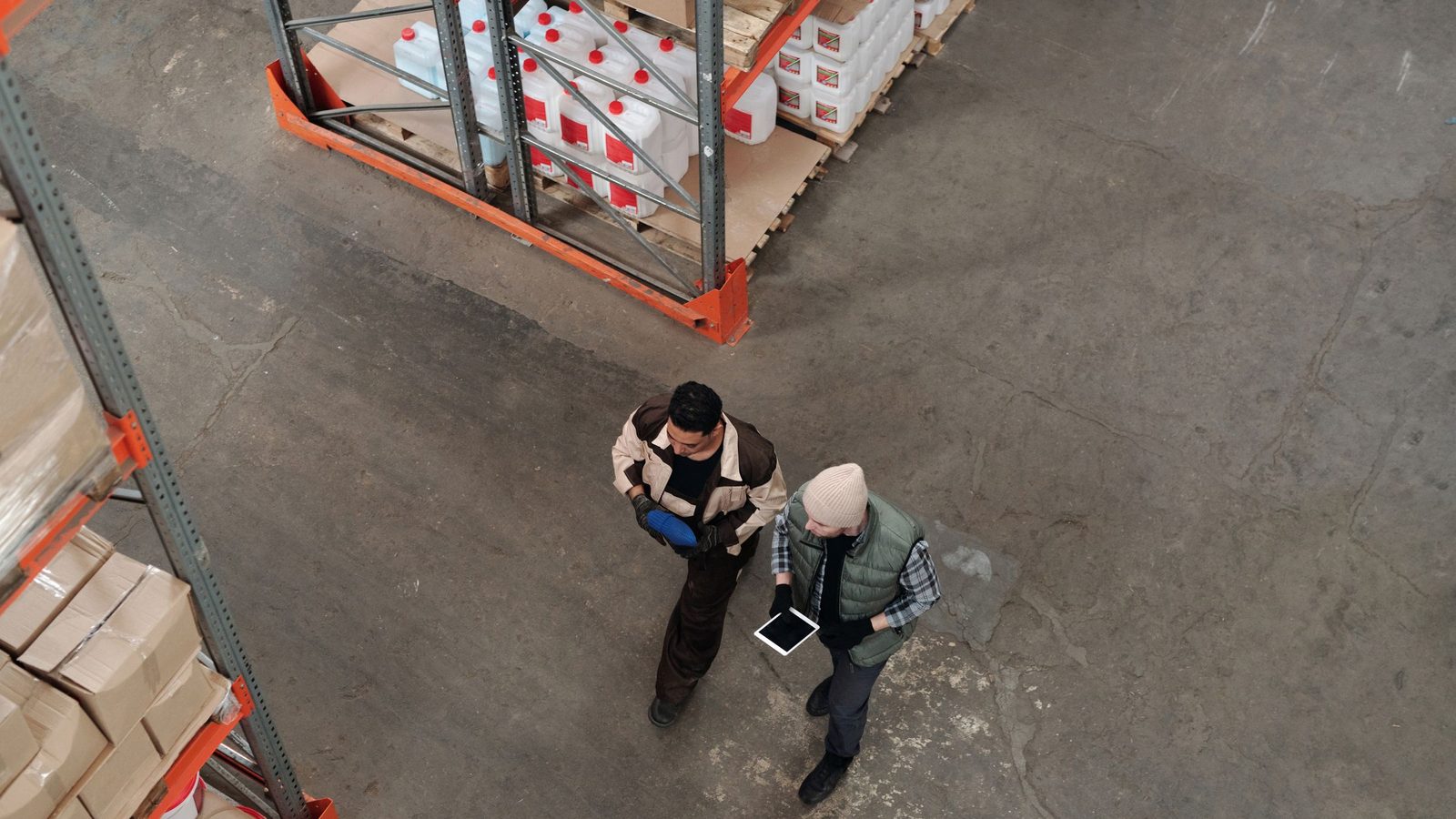 Two workers discussing inventory in a warehouse, using a digital tablet for coordination