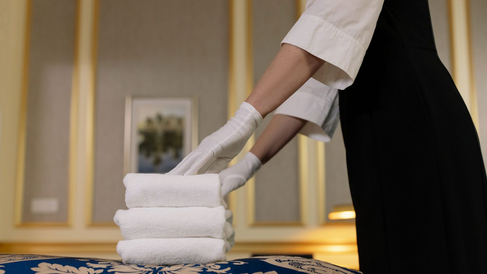 A hotel housekeeper neatly stacks fresh towels in a luxurious room setting