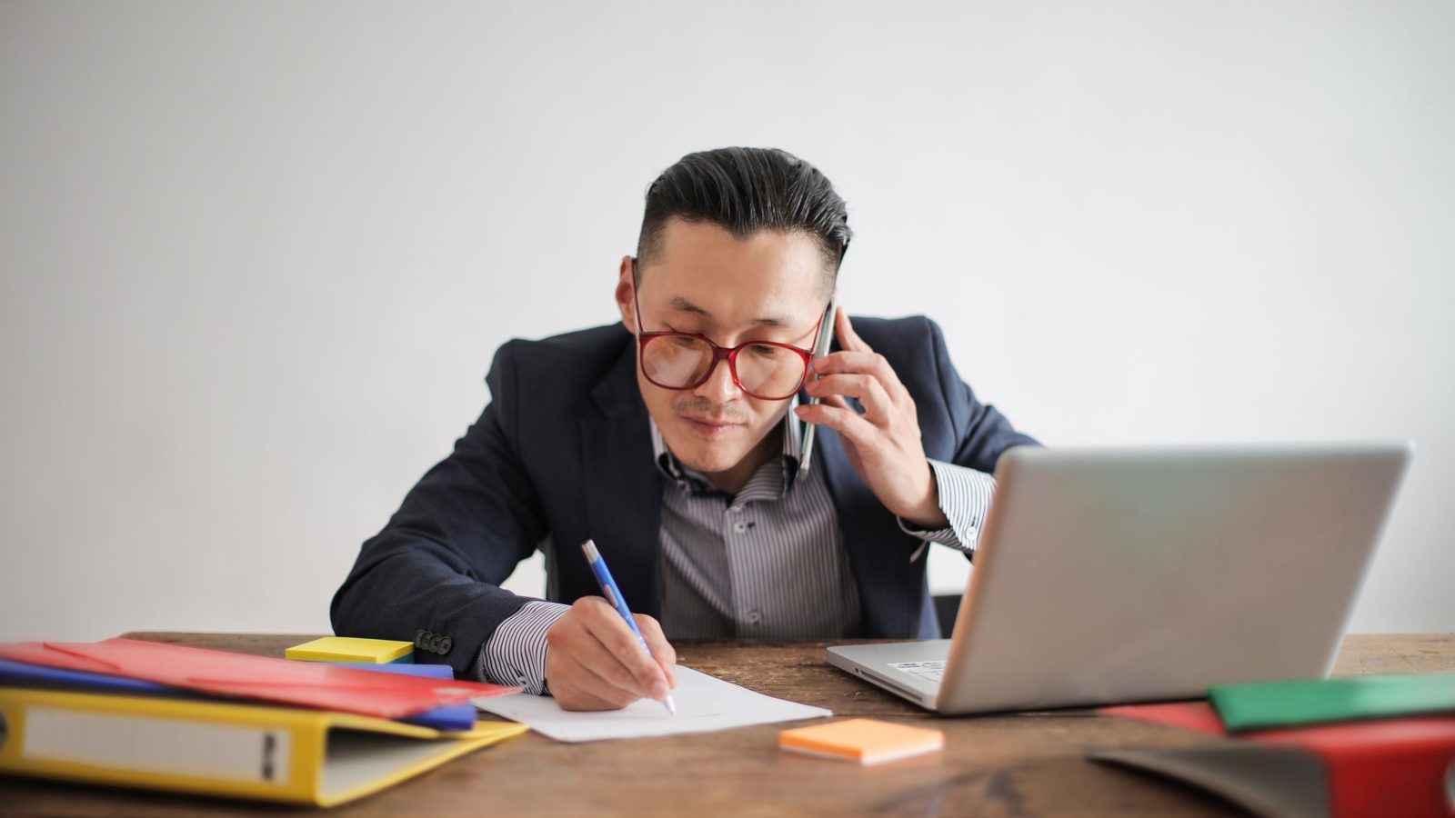 Professional businessman multitasking with phone call and laptop while writing notes at desk