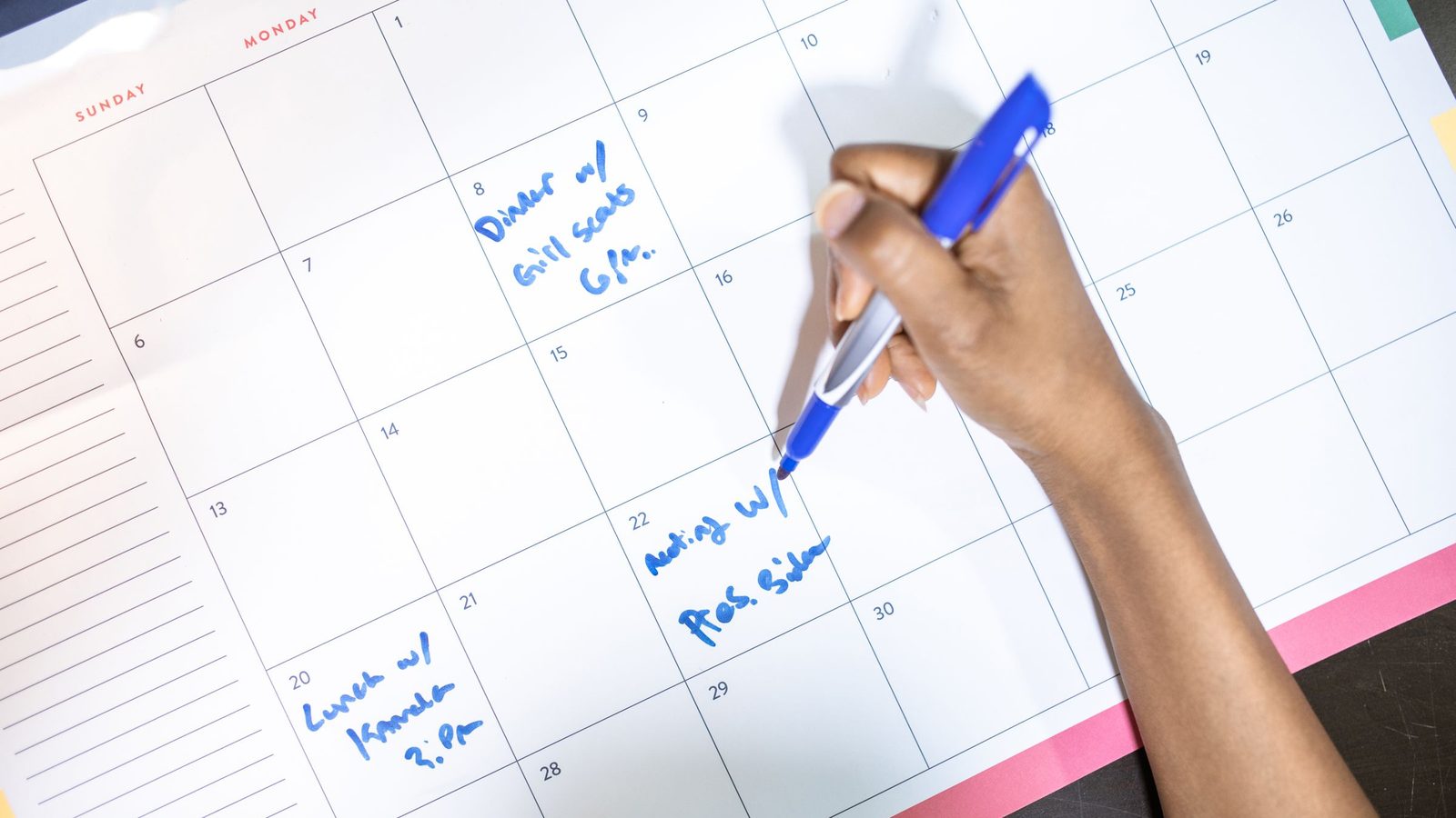 Person writing appointments on a wall planner with a blue pen