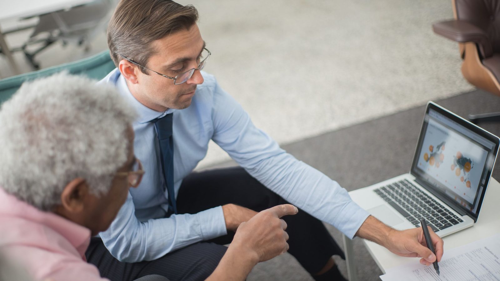Two men in a business meeting reviewing financial documents and discussing data on a laptop