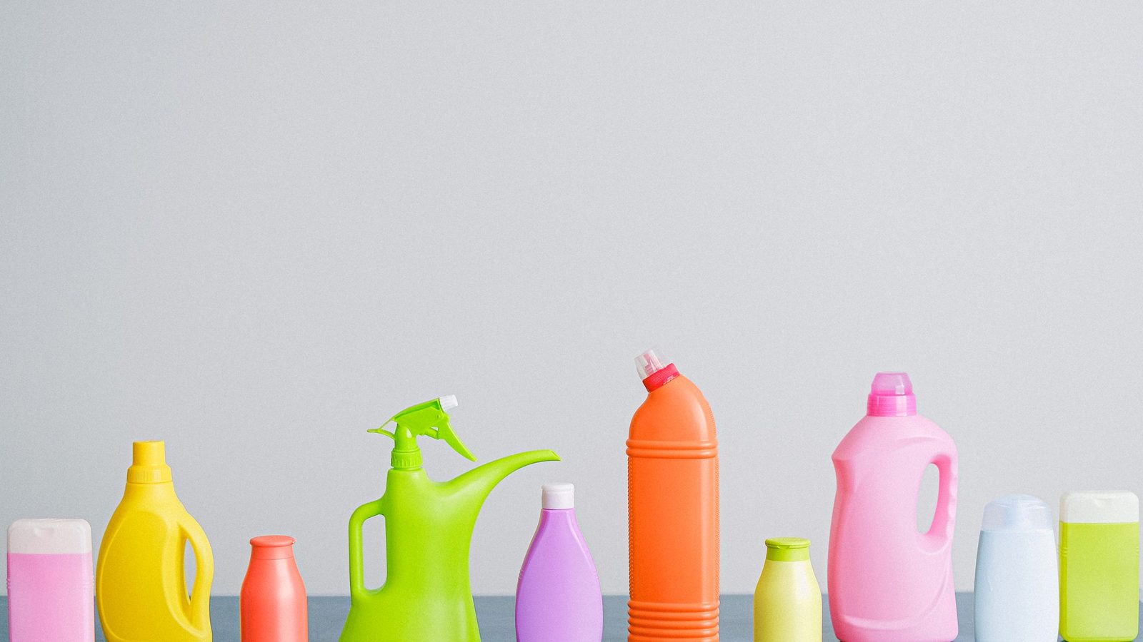 Arrangement of colorful plastic bottles with assorted cleaning products for household placed on table in row against white background in light studio