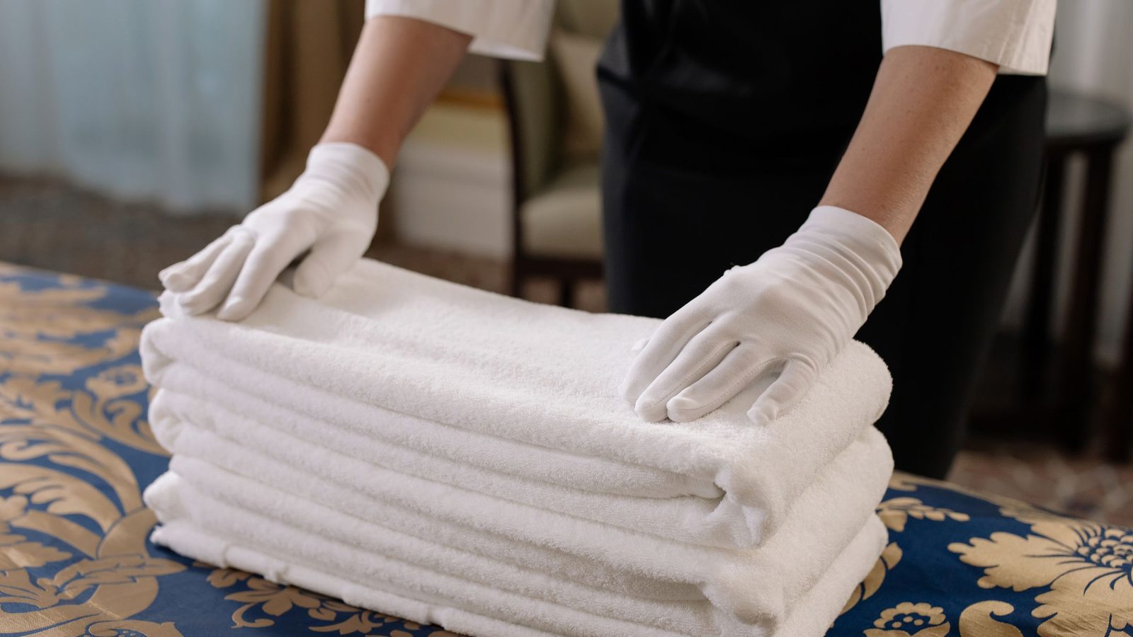 Professional housekeeper folding clean towels on a bed in a hotel room, emphasizing neatness and service