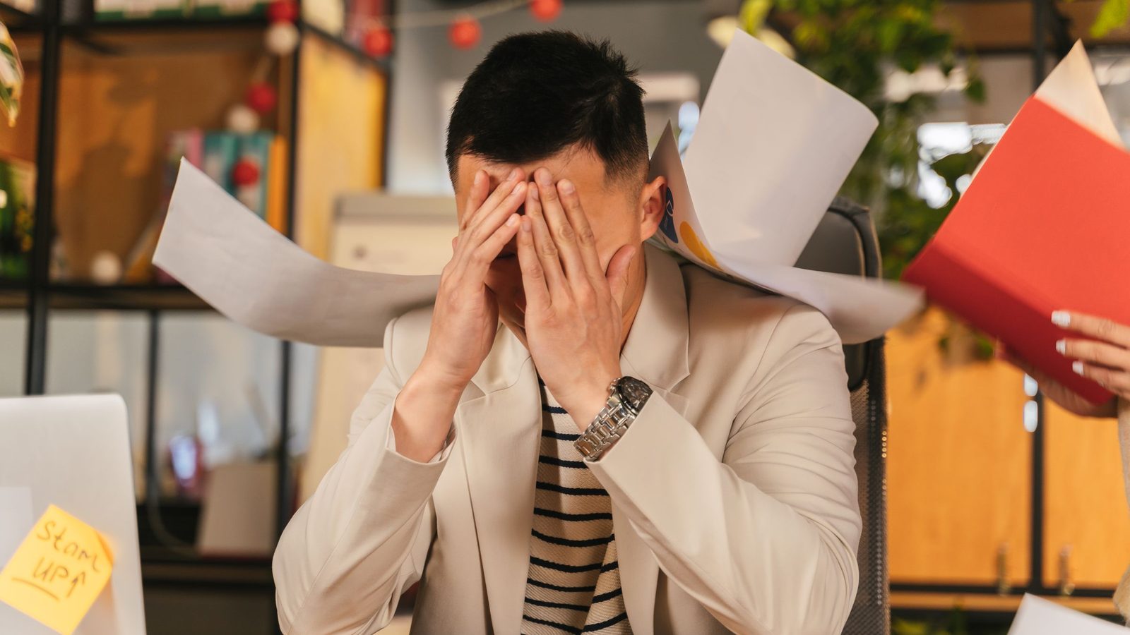 Stressed businessman overwhelmed by paperwork in office environment, demonstrating burnout