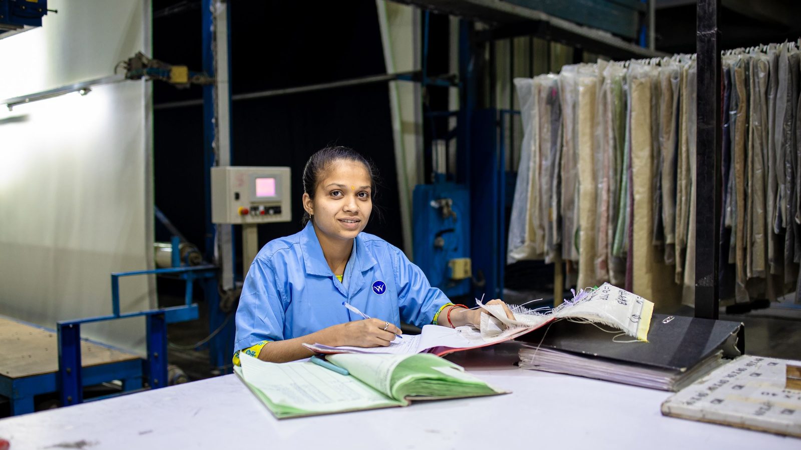 Female textile worker in factory reviewing documents at a desk