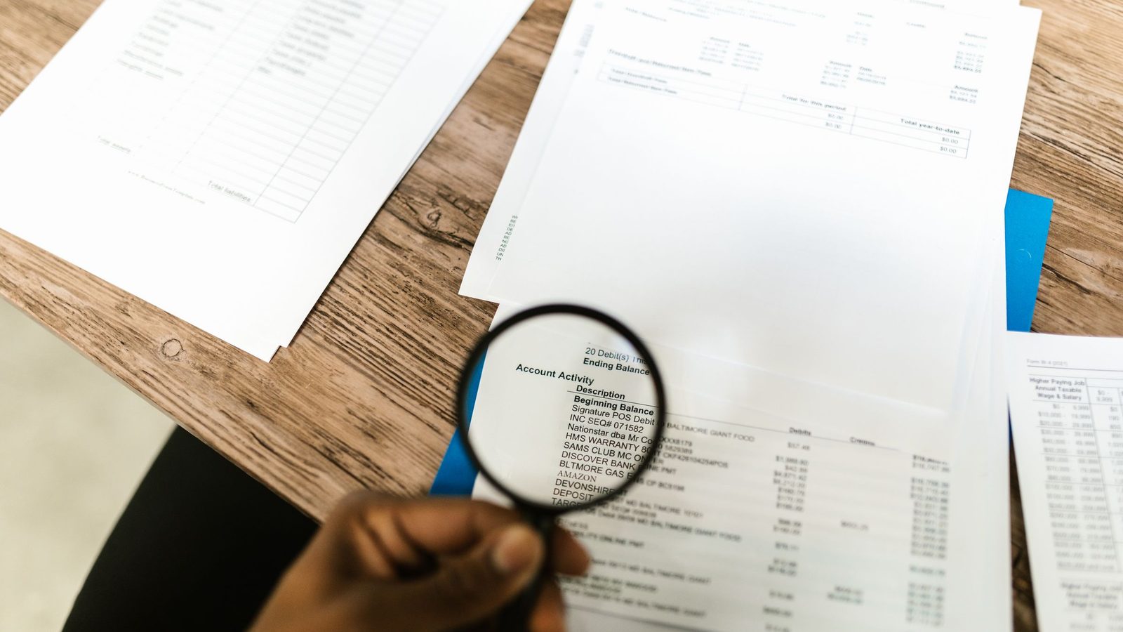 Close-up of hand using magnifying glass to review documents